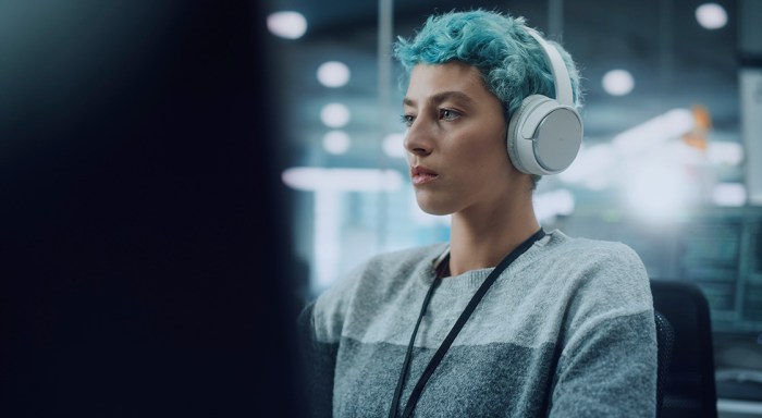 A woman on a chair wearing headphones and looking at a desktop screen