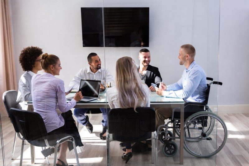 Group Equality Policy: a group of workers sitting at a table talking, one of them in a wheelchair