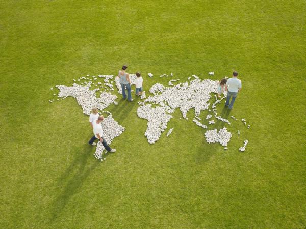 People walking on a world map made of stones on grass, symbolizing global connection and supply chain sustainability.