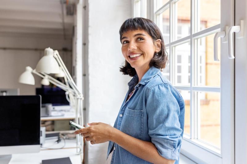 Smiling professional with mobile phone in a bright office.