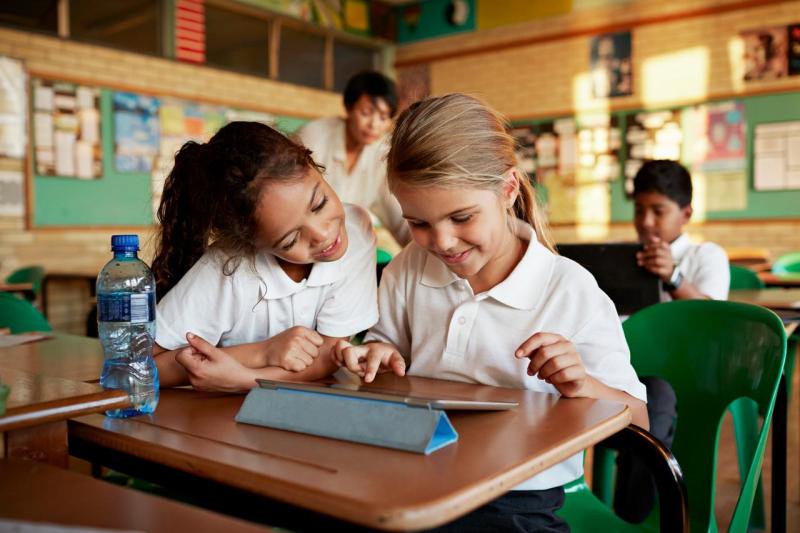 Dos niñas aprenden juntas con una tablet en el aula, reflejando cómo la tecnología impulsa la curiosidad y el aprendizaje colaborativo según el Informe de la Fundación Telefónica.