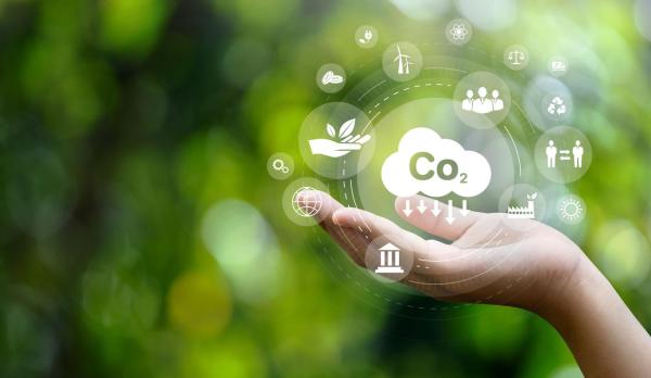 Una persona toca el icono de CO₂ en una pantalla digital, simbolizando la descarbonización y la reducción de gases de efecto invernadero gracias a las TIC.